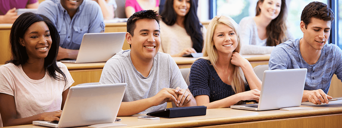 Lifestyle image of students at a lecture with open laptops. They look enthusiatic and are smiling, possibly laughing