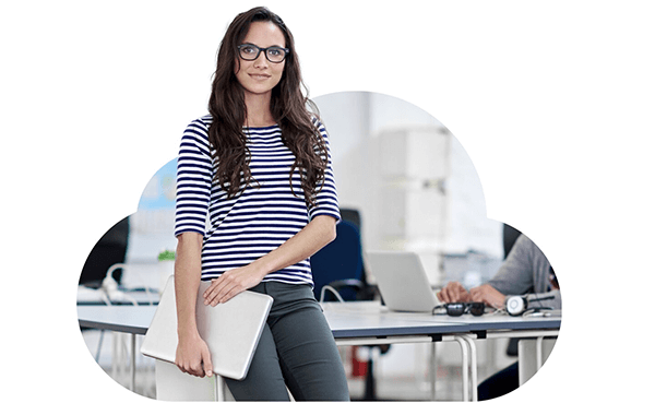 image of a bespectacled woman with perched on the corner of a desk, holding her laptop pc